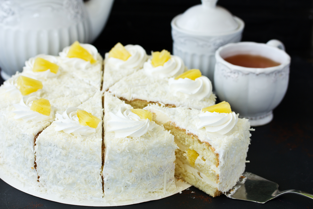 bolo de abacaxi fatiado em cima de uma mesa preta, com uma xícara branca de chá ao fundo