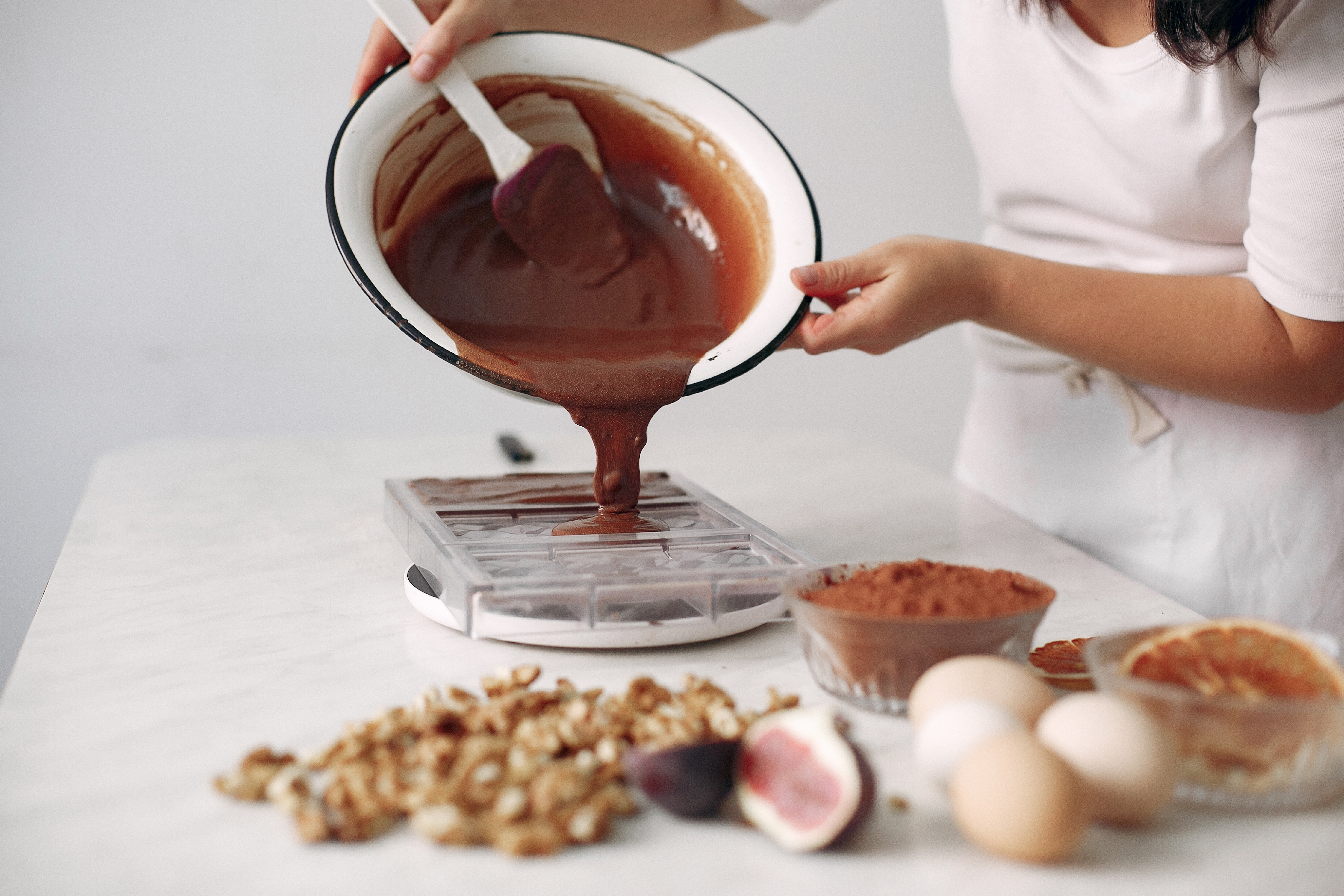 Mulher confeiteira despejando massa de bolo de chocolate sobre uma forma.