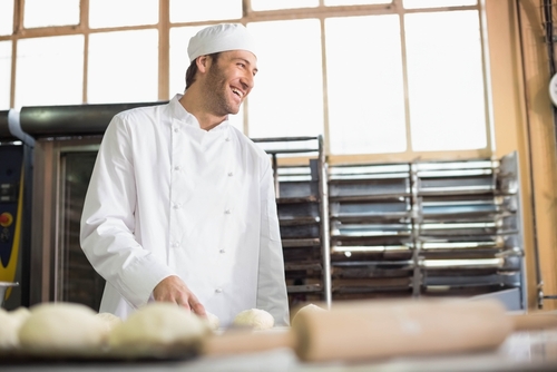 Profissional de culinária sorrindo em setor de produção de padaria