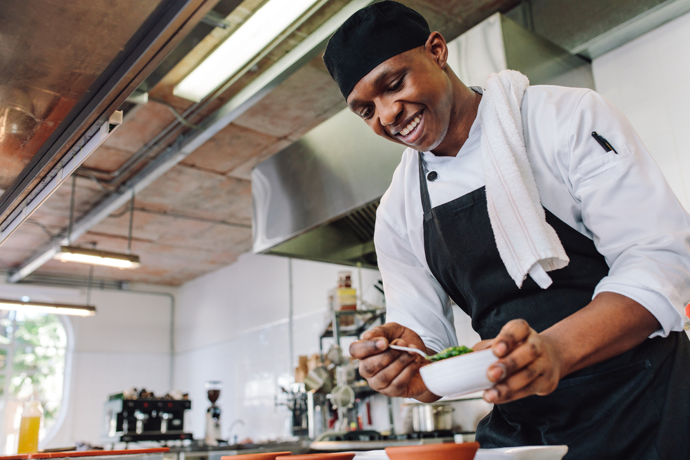 chef de cozinha negro sorrindo e finalizando um prato em sua cozinha