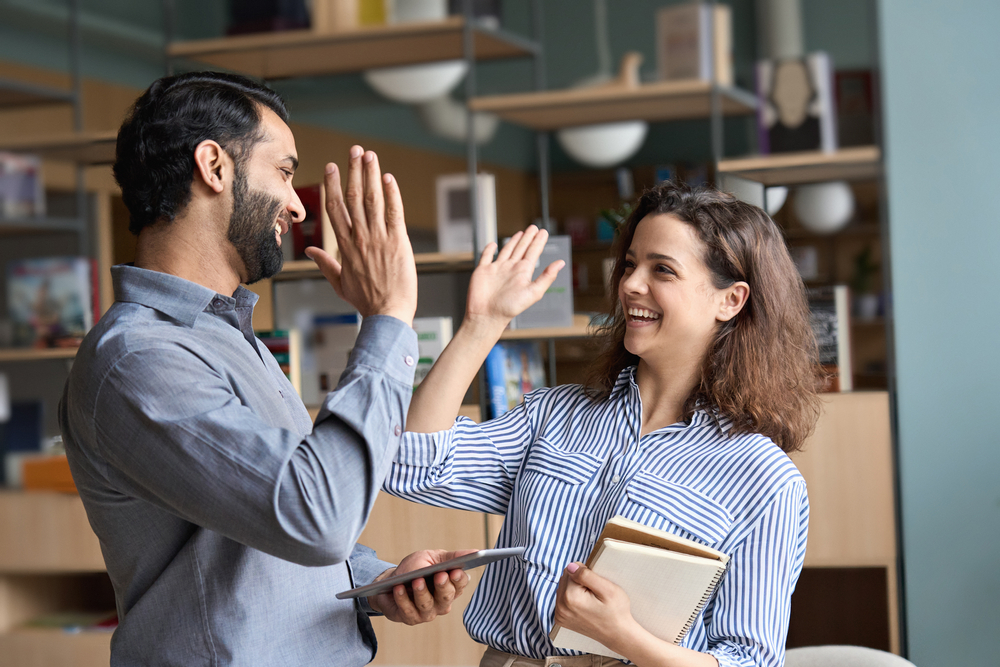 Um homem e uma mulher em ambiente profissional. Ambos felizes e comemorando o sucesso, batendo com as mãos em resultado de cooperação e trabalho em equipe