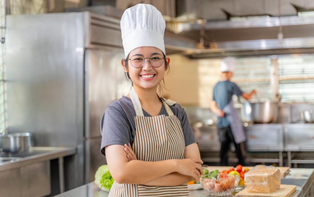 Jovem profissional de culinária sorrindo em cozinha profissional